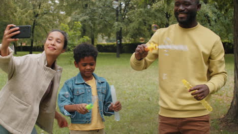 Glückliche-Afroamerikanische-Familie-Bläst-Seifenblasen-Und-Macht-Selfie-Im-Park